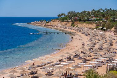 Sharm El Sheikh, Mısır - 25 Mayıs 2021: İnsanlar Sharm El Sheikh, Mısır, Afrika 'daki Kızıldeniz kıyısındaki bir tropik tatil beldesinde plaj sandalyeleri ve saman şemsiyeleriyle lüks bir kumsalda dinleniyorlar.