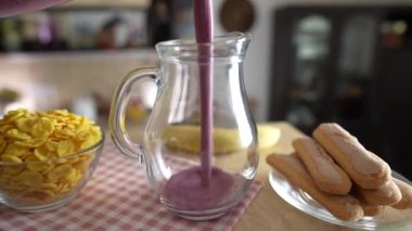 Mutfaktaki dönen bir masada şeffaf cam bir kavanoza taze meyve suyu dökerek, kapat. Lezzetli yaban mersini, muz, bal ve süt karışımı.