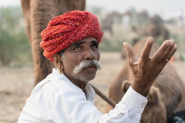 Pushkar, Hindistan - 15 Kasım 2018: Hindistan 'ın kutsal şehri Pushkar, Rajasthan yakınlarındaki Pushkar Camel Mela sırasında çölde yaşayan Hintli erkek ve deve. Bu fuar dünyanın en büyük deve ticaret fuarı.