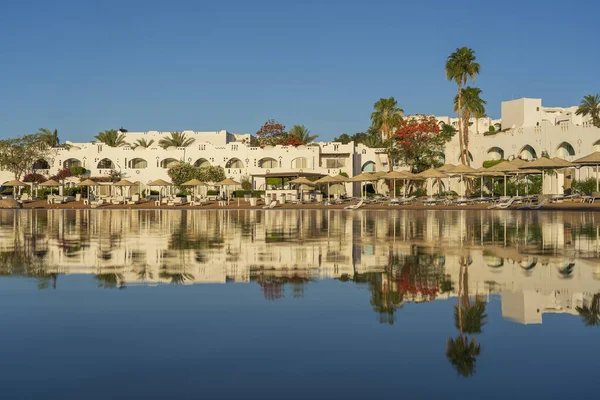 Gündoğumunda, Mısır 'ın Sharm El Sheikh tatil beldesindeki sakin deniz suyuna binalar, güneşlikler ve şemsiyeler yansıtılır.