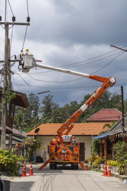 Koh Phangan, Tayland - Jan, 26, 2022: Gezici vinç kovasında duran iki erkek elektrikçi Tayland 'ın Koh Phangan adasındaki elektrik hattının kablosunu tamir ediyor