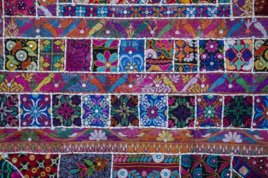 Hindistan 'ın arka planındaki renkli halının detaylarını anlat. Bir tuvale dikilmiş çeşitli kumaş parçalarını kapat