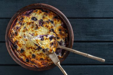 Yabanmersinli süzme peynir güveci, yakın çekim. Siyah masada taze böğürtlenli kremalı güveç. Üst görünüm
