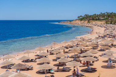 Sharm El Sheikh, Mısır - 25 Mayıs 2021: İnsanlar Sharm El Sheikh, Mısır, Afrika 'daki Kızıldeniz kıyısındaki bir tropik tatil beldesinde plaj sandalyeleri ve saman şemsiyeleriyle lüks bir kumsalda dinleniyorlar.