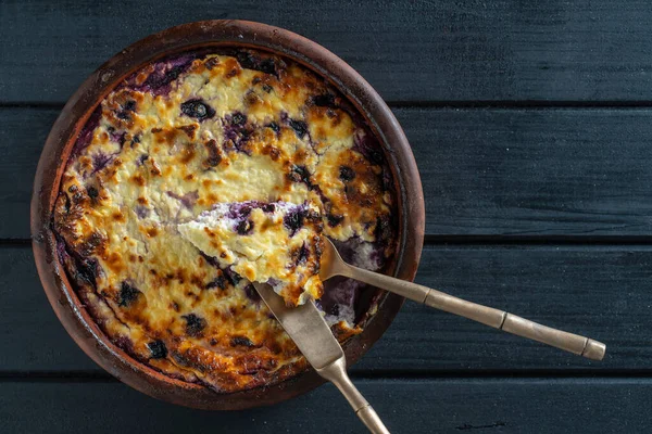 Yabanmersinli süzme peynir güveci, yakın çekim. Siyah masada taze böğürtlenli kremalı güveç. Üst görünüm