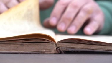 Evde ya da kütüphanede kitap okuyan bir adamın eli. Eski bir kitabın sayfalarını çevirip kapat.