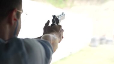 Adam atış poligonundaki hedeflere tabancayla ateş ediyor. Yaklaş, bulanık odaklan. Atış talimi yaparken arkadan ateş eden bir adamın görüntüsü. Yavaş çekim