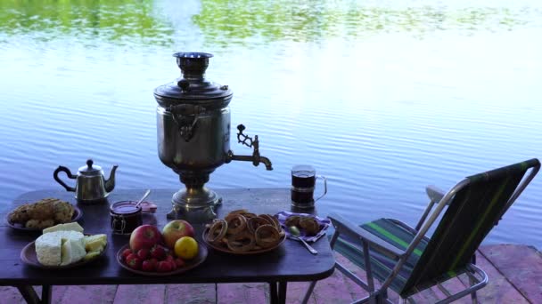 白煙と朝 ウクライナの緑の森の中の穏やかな水の湖の近くのテーブルの上の食品とヴィンテージ金属茶サモヴァール 自然食の概念 — ストック動画