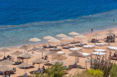 Sharm El Sheikh, Mısır - 25 Mayıs 2021: İnsanlar Sharm El Sheikh, Mısır, Afrika 'daki Kızıldeniz kıyısındaki bir tropik tatil beldesinde plaj sandalyeleri ve saman şemsiyeleriyle lüks bir kumsalda dinleniyorlar.