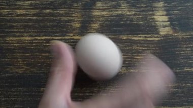 Chicken egg rotates on a wooden table, close up, top view