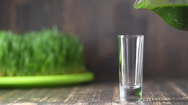 Yeşil filizlenmiş buğday tanelerinin çimenlerinden sağlıklı organik yeşil detoks suyu, yakın çekim, yavaş çekim. Taze buğday yaprakları ve buğday suyu bir bardağa dökülüyor.