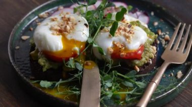 Bread toast, poached eggs, avocado pulp, pea microgreens  and fresh vegetables on plate in cafe, close up, rotates, breakfast time