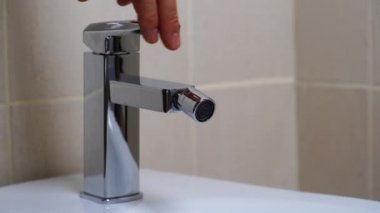 Modern banyodaki bej kaplamalı musluktan akan su ile birlikte beyaz seramik bidet detayları. Basit stil ve modern ev dekorasyonu. Kapat.