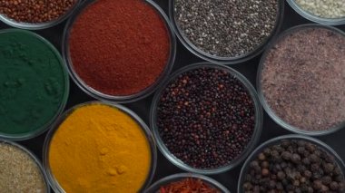 Arka planda farklı baharatlar ve bitkiler dönüyor, yakın plan, üst görünüm. Renkli baharatlar, tohumlar ve yemek pişirmek için bitkiler.