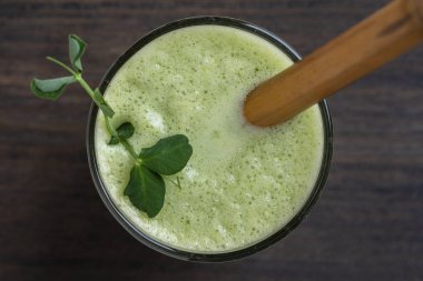 Bir bardak yeşil smoothie, ahşap arka planda yapraklı bezelye mikroyeşilliği ile süslenmiş, yakın plan. Vejetaryen ve sağlıklı beslenme konsepti. Organik yiyecekler. Üst görünüm