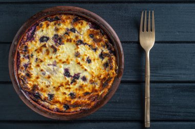 Yabanmersinli süzme peynir güveci, yakın çekim. Siyah masada taze böğürtlenli kremalı güveç. Üst görünüm