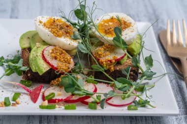 Ekmek tostu, haşlanmış yumurta, avokado dilimi, bezelye mikroçerezi ve taze turp bir kafede, yakın plan kahvaltı zamanı.