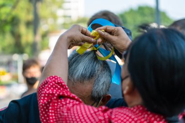 Bangkok, Thailand - Feb, 27, 2022 : Thai woman ties Ukrainian flag-colored ribbons on a man's hair during a demonstration against Russian interference in Ukraine in Bangkok, Thailand