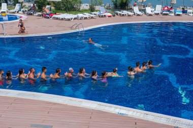 Didim, Türkiye - Eylül 2019: İnsanlar Didim, Türkiye 'deki tatil otelinin deniz kenarındaki yüzme havuzunda aerobik yapıyor, yüzüyor ve güneşleniyor. Tatil ve eğlence kavramı