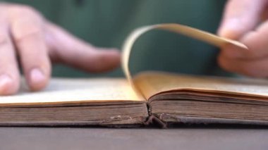 Evde ya da kütüphanede kitap okuyan bir adamın eli. Eski bir kitabın sayfalarını çevirip kapat.
