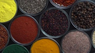 Arka planda farklı baharatlar ve bitkiler dönüyor, yakın plan, üst görünüm. Renkli baharatlar, tohumlar ve yemek pişirmek için bitkiler.