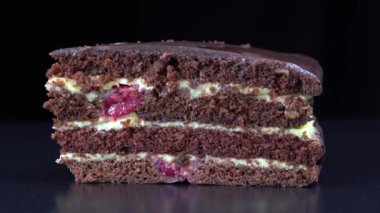 Delicious dark chocolate cream cake from short pastry with custard and cherry berry in the home kitchen. Piece of dark chocolate cake on the black background rotating. Homemade baking. Close up