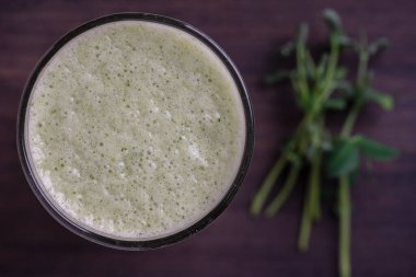 Bir bardak yeşil smoothie, ahşap zemin üzerinde yapraklı bezelye mikroyeşilliklerinden, yakın çekim. Vejetaryen ve sağlıklı beslenme konsepti. Organik yiyecekler. Üst görünüm