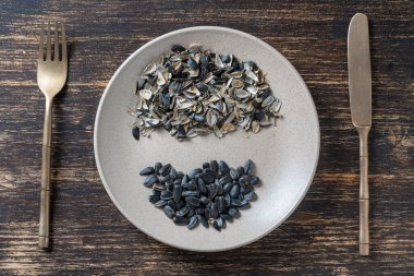 Ayçekirdeği çekirdeği, ay çekirdeği kabuğu, bir tabak içinde çatal ve bıçakla birlikte ahşap bir arka planda, üst manzara, kapat.