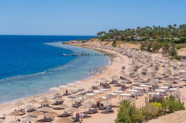 Sharm El Sheikh, Mısır - 25 Mayıs 2021: İnsanlar Sharm El Sheikh, Mısır, Afrika 'daki Kızıldeniz kıyısındaki bir tropik tatil beldesinde plaj sandalyeleri ve saman şemsiyeleriyle lüks bir kumsalda dinleniyorlar.