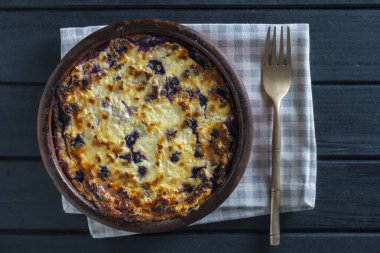 Yabanmersinli süzme peynir güveci, yakın çekim. Siyah masada taze böğürtlenli kremalı güveç. Üst görünüm