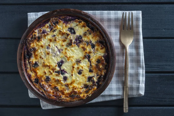 Yabanmersinli süzme peynir güveci, yakın çekim. Siyah masada taze böğürtlenli kremalı güveç. Üst görünüm