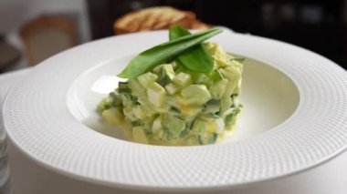 Beyaz tabak, sarımsak, salatalık, haşlanmış yumurta ve ekşi krema salatası. Mutfaktaki masada döner.