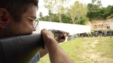 Man shoots with a combat shotgun at targets on the shooting range, close up, slow motion. Back view of man shooting shotgun at target while practicing