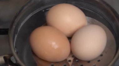 Three fresh chicken eggs boiling in stainless steel pan with sound, close up, top view