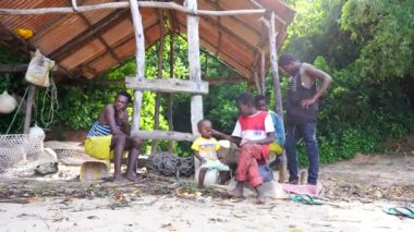 Zanzibar, Tanzanya - 16 Kasım 2019: Afrikalı erkek ve çocuklar Zanzibar, Tanzanya, Doğu Afrika kıyılarındaki gölgelerde bir gölgelik altında oturuyorlar.