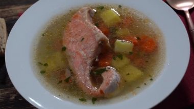 Fresh salmon fish soup with carrots, potatoes and herbs in a white plate, close up, rotates.Tasty dinner consists of a fish soup with salmon