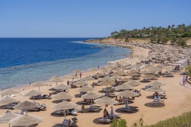 Sharm El Sheikh, Mısır - 25 Mayıs 2021: İnsanlar Sharm El Sheikh, Mısır, Afrika 'daki Kızıldeniz kıyısındaki bir tropik tatil beldesinde plaj sandalyeleri ve saman şemsiyeleriyle lüks bir kumsalda dinleniyorlar.