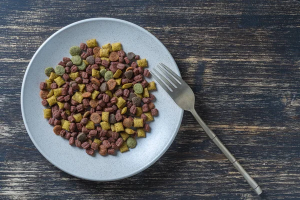 Ahşap zemin çatallı tabakta kurutulmuş kedi maması, üst manzara, kapat.