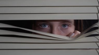Close up front portrait from indoors of young girl pushing blinds at window with hands. Looking fearfully outside at night