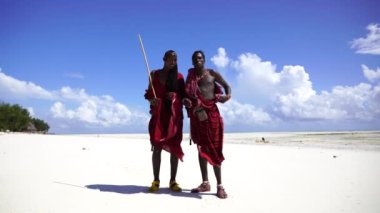 Zanzibar, Tanzanya - 12 Aralık 2019: Geleneksel kıyafetler giymiş iki Afrikalı adam okyanus kenarında, Tanzanya, Doğu Afrika 'daki Zanzibar adasının kumsalında duruyor.