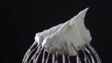 Kırbaçlanmış yumurta beyazı ile metal çırpma, siyah arka planda izole edilmiş, yakın plan, döner