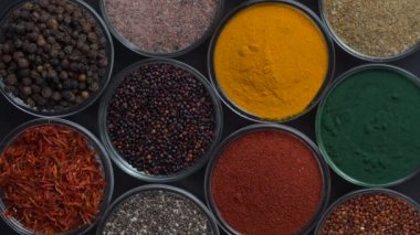 Arka planda farklı baharatlar ve bitkiler dönüyor, yakın plan, üst görünüm. Renkli baharatlar, tohumlar ve yemek pişirmek için bitkiler.