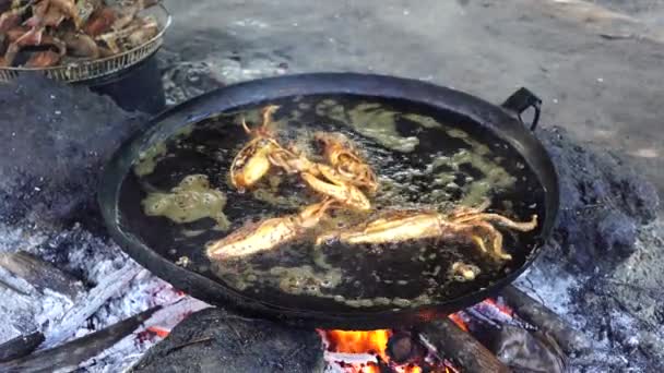 売り手は タンザニアのザンジバル島 東アフリカの地元のストリートフード市場で開かれた火の上に大きなフライパンで野菜油で販売のためのイカを炒めます 閉じろ — ストック動画