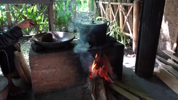 地元のバリの家 ウブド バリ島 インドネシアの島で火の上に陶器の鍋で老婦人ローストコーヒー穀物 台所の粘土鍋で焙煎したコーヒー豆 — ストック動画