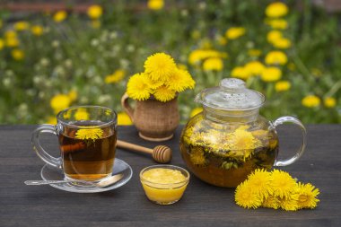 Bahçedeki ahşap masada ballı taze karahindiba çiçeklerinden yapılmış lezzetli bitki çayı, yakın plan. Karahindiba çayı, cam çaydanlık ve fincanda