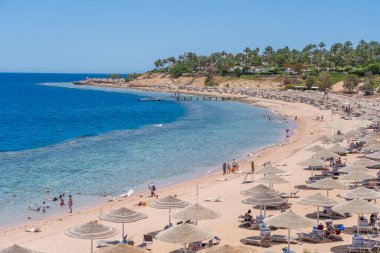 Sharm El Sheikh, Mısır - 25 Mayıs 2021: İnsanlar Sharm El Sheikh, Mısır, Afrika 'daki Kızıldeniz kıyısındaki bir tropik tatil beldesinde plaj sandalyeleri ve saman şemsiyeleriyle lüks bir kumsalda dinleniyorlar.