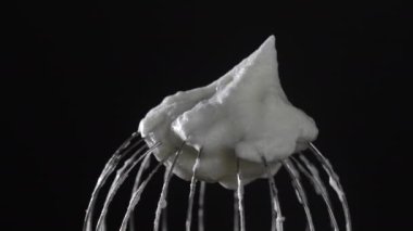 Kırbaçlanmış yumurta beyazı ile metal çırpma, siyah arka planda izole edilmiş, yakın plan, döner