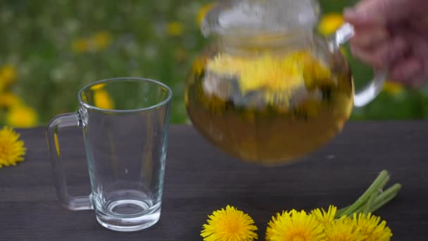 美味的香草茶 由新鲜的蒲公英花制成 放在春天花园的木制桌子上 关门了 玻璃壶中的蒲公英热茶和自然背景下的杯子 — 图库视频影像