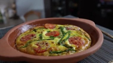 Sebzeli frittata ile seramik kase, basit vejetaryen yemeği. Yumurtalı frittata, domates, biber, soğan, peynir ve yeşil sarımsak yaprakları masada, döndür, kapat. Sağlıklı yumurta omleti.