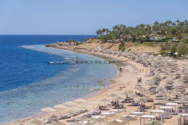 Sharm El Sheikh, Mısır - 25 Mayıs 2021: İnsanlar Sharm El Sheikh, Mısır, Afrika 'daki Kızıldeniz kıyısındaki bir tropik tatil beldesinde plaj sandalyeleri ve saman şemsiyeleriyle lüks bir kumsalda dinleniyorlar.
